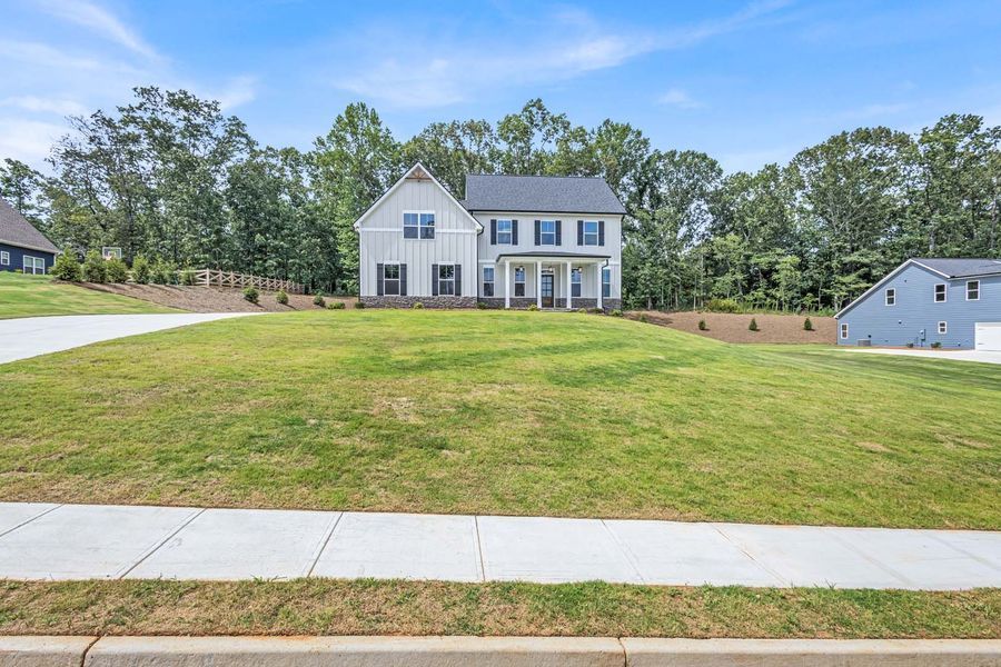 Two-story light gray house with blue shutters, green lawn, and trees under a blue sky.