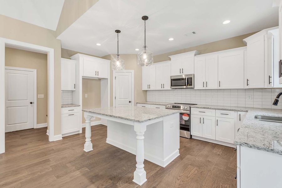 White kitchen with island, cabinets, appliances, hardwood floors, and two pendant lights.
