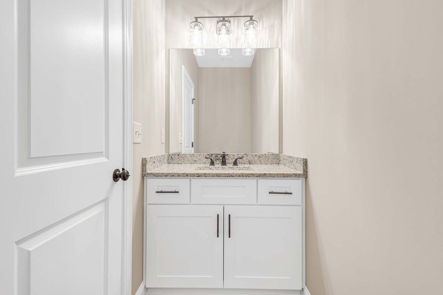 White bathroom vanity with mirror, overhead lights, and closed door.