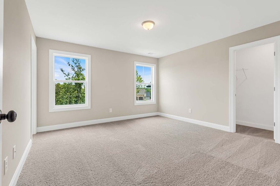 Empty bedroom with beige walls, two windows, and a doorway to the right.