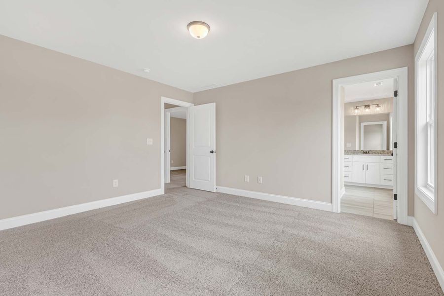 Empty bedroom with beige walls, carpet, and a doorway to a bathroom.