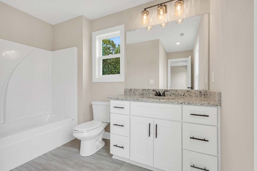 White bathroom with bathtub, toilet, vanity, mirror, and window. Gray floor and light beige walls.
