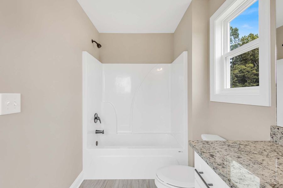 Bathroom with white tub and toilet, granite counter, window with blue sky.