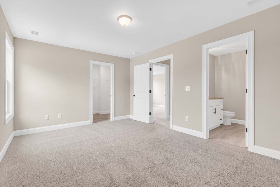 Empty beige-walled bedroom with three doorways and a neutral carpet.