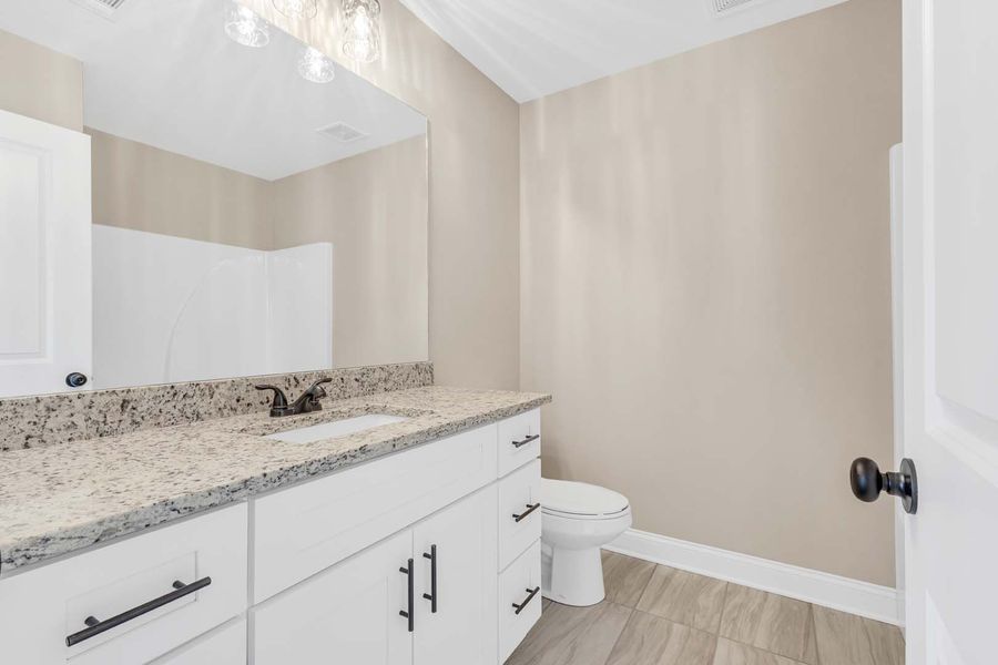 Bathroom with white cabinets, granite countertop, toilet, and beige walls.