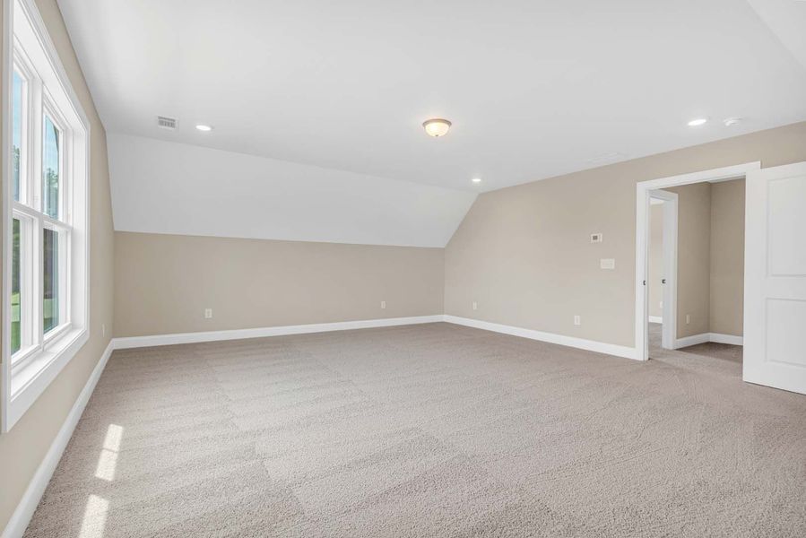 Empty, beige carpeted room with a sloped ceiling, window, and open doorway.