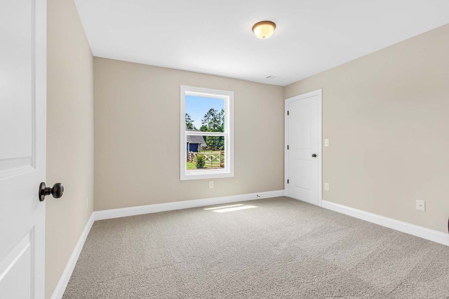 Empty beige bedroom with a window, door, and gray carpet.