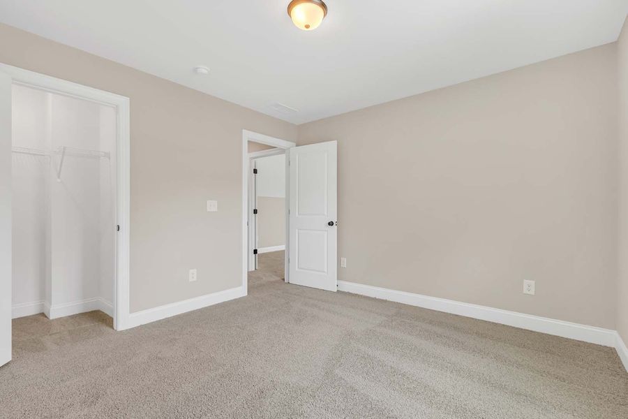 Empty bedroom with beige walls, white trim and doors, and gray carpet.