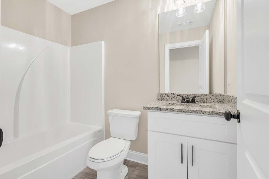 Bathroom with white tub, toilet, vanity, and neutral walls.