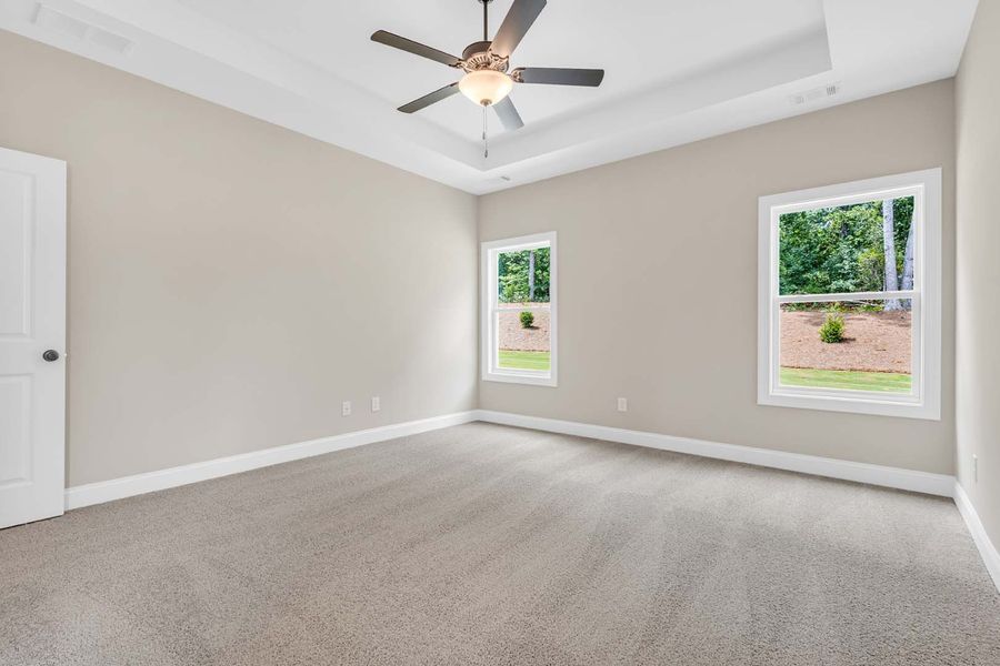 Empty bedroom with neutral walls, two windows, and gray carpet. Ceiling fan.