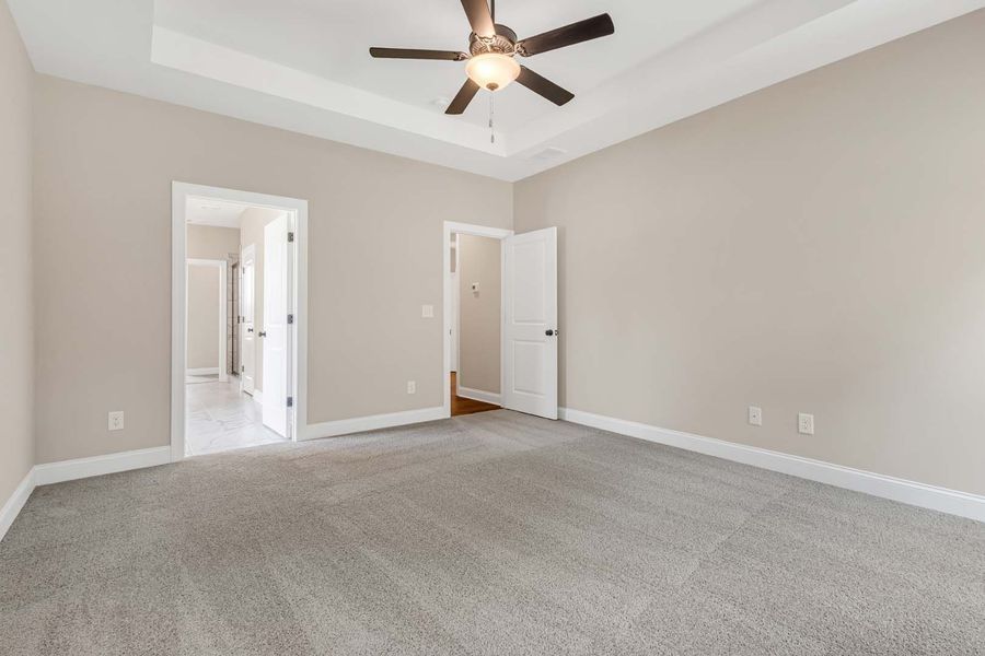 Empty bedroom with gray carpet, beige walls, and white doors.