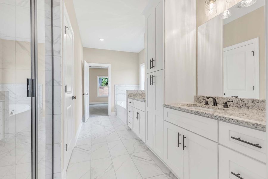 White bathroom with shower, vanity, cabinets, and marble tile floor.