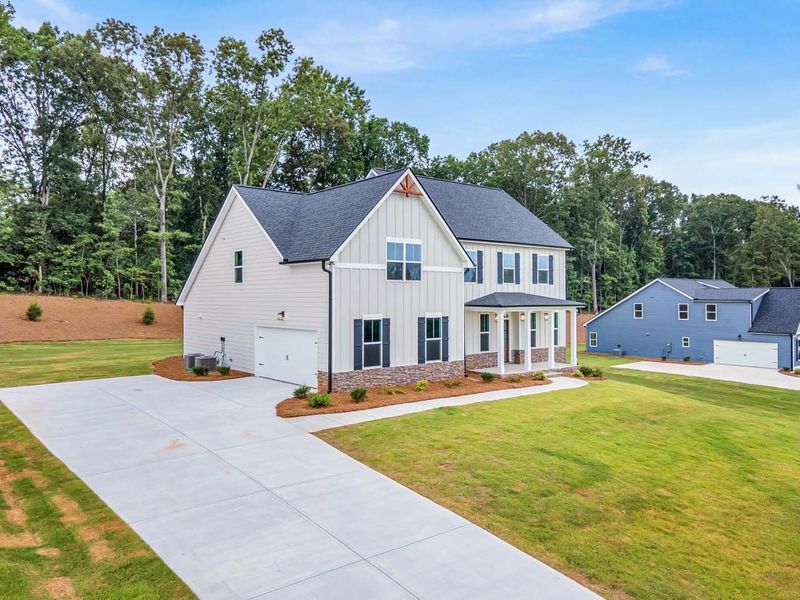 Two-story house with light siding, black shutters, and a concrete driveway on a green lawn.