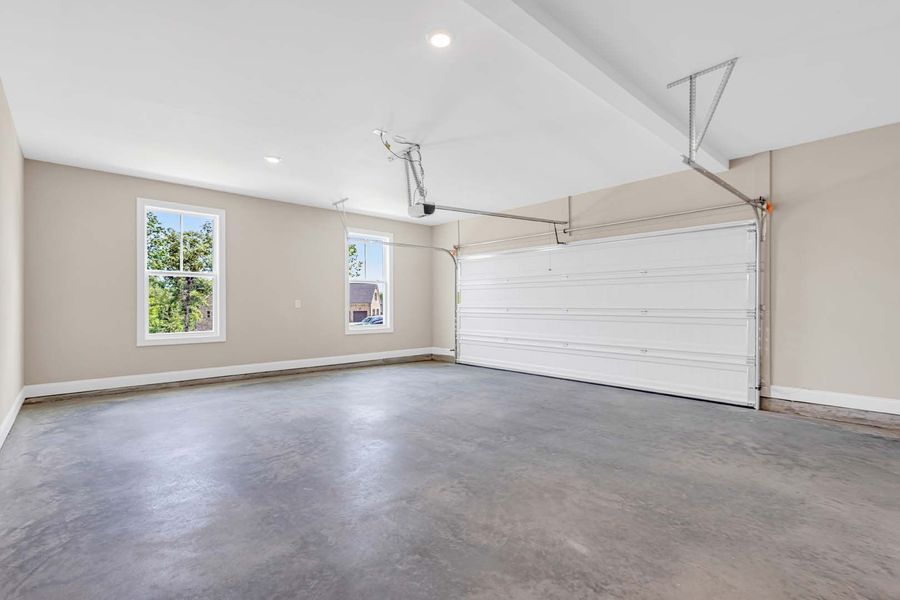 Empty garage with gray concrete floor, white garage door, and two windows.