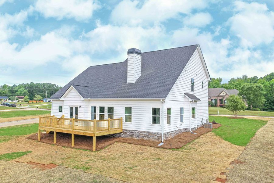 White house with wooden deck, set on a grassy lot with blue sky and clouds.