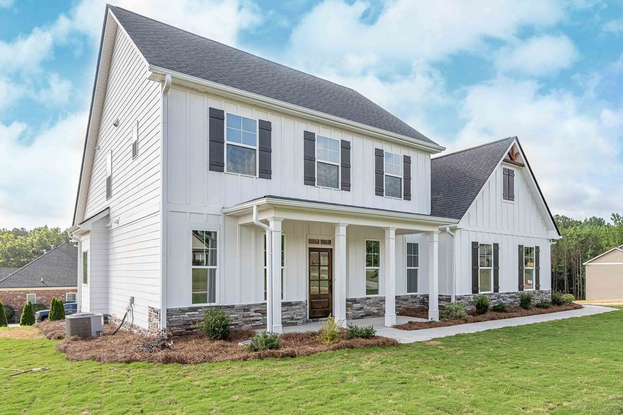 White farmhouse-style home with black shutters and a stone base; on a green lawn, cloudy sky.