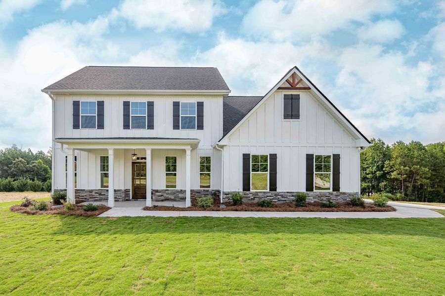 Two-story white farmhouse with black shutters and stone accents, on a green lawn under a blue sky.
