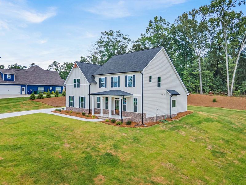 Two-story white house with black shutters, set on a grassy lawn near trees.