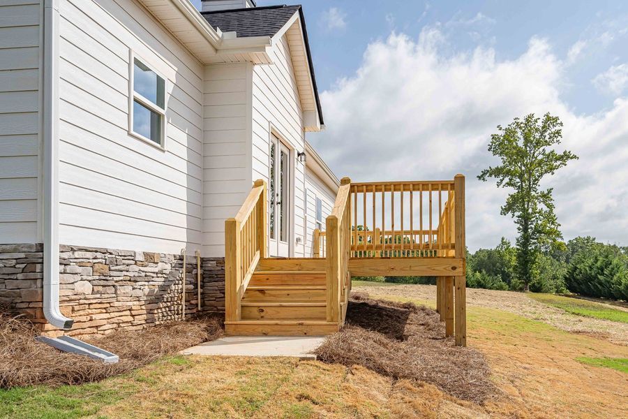 Wooden deck with stairs leading to a white house. A grassy yard and a cloudy sky are in the background.
