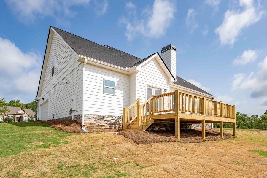 White house with wooden deck and black roof against a blue sky with clouds.