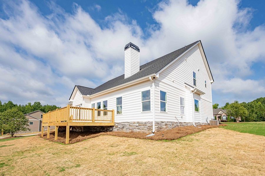White farmhouse with a wooden deck under a cloudy blue sky.