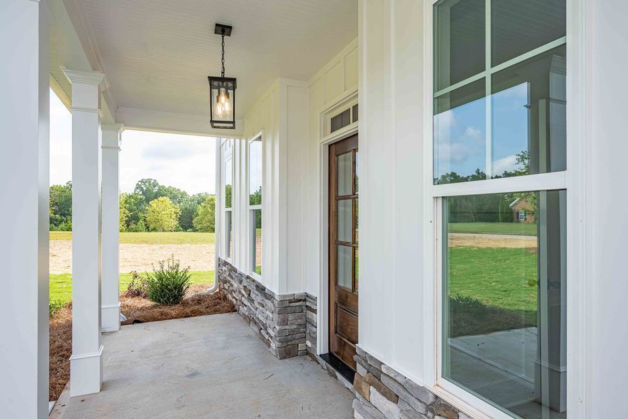 Covered porch with white columns, a brown door, and large windows overlooking a yard.