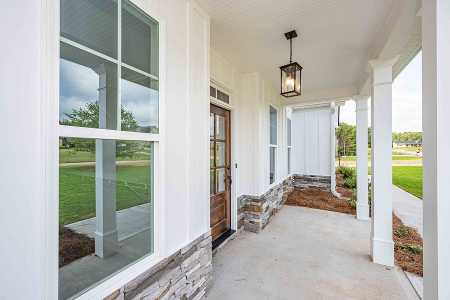 White porch with large windows and a brown door, accented by stone and a hanging light.
