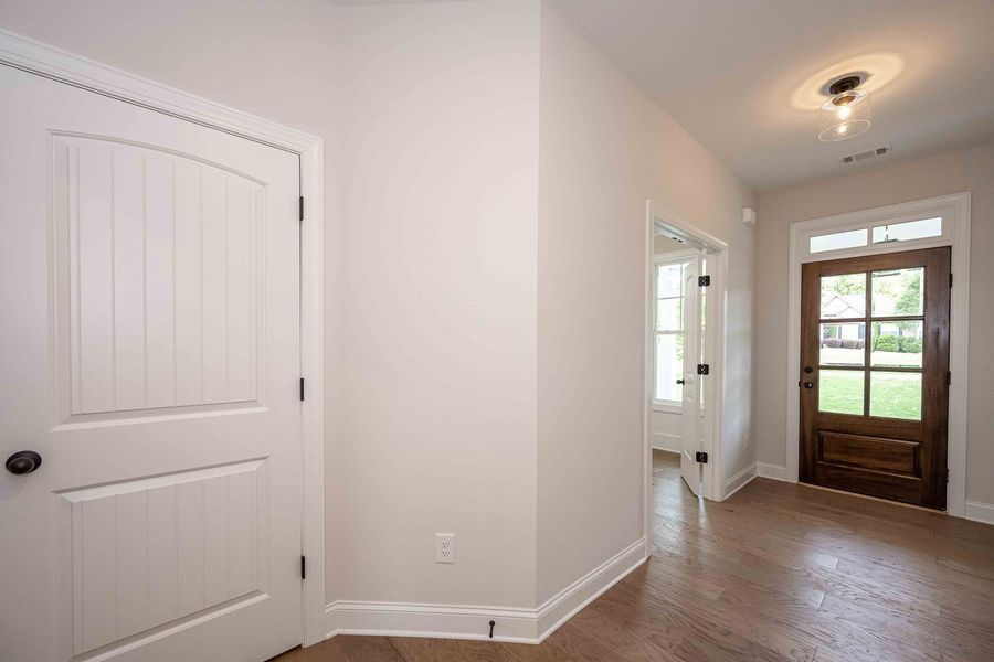 Interior hallway with white walls, wood floor, and a brown front door with windows.
