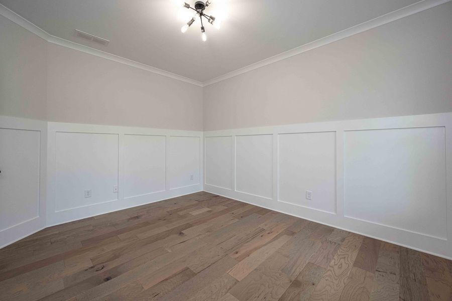 Empty room with white paneled walls, light wood floors, and a ceiling light.