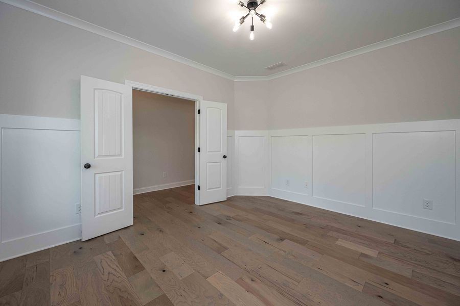 Empty room with light wood floors, white paneling and doors, beige walls, and a small ceiling light.