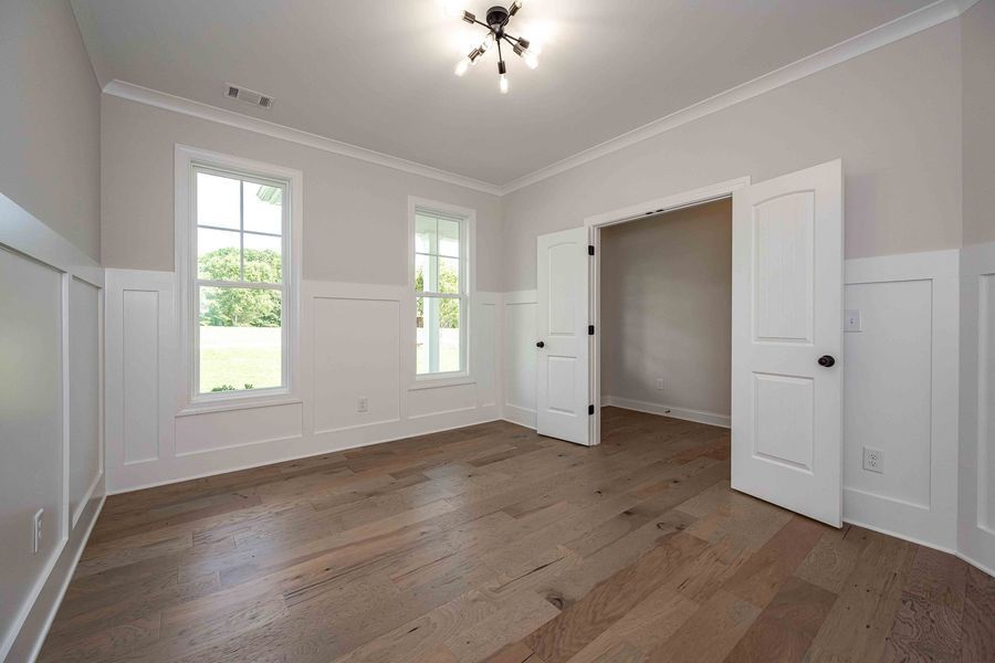 Empty room with light wood floors, white wainscoting, two windows, and open doorway.