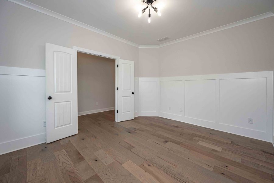 Empty room with light wood floors, white trim and doors, and beige walls.