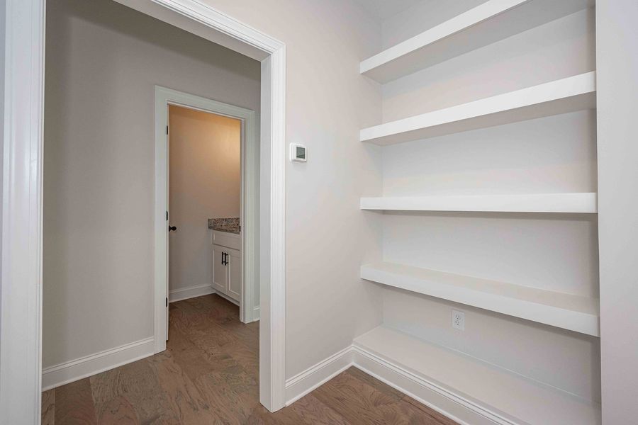 White pantry with built-in shelves and an open doorway leading to a bathroom with a sink.