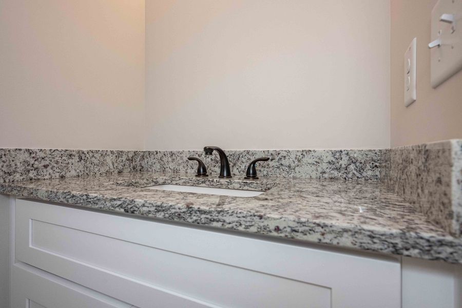 White bathroom vanity with granite countertop and black faucet.