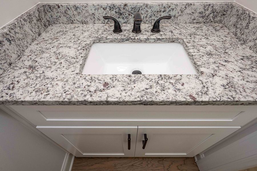 White bathroom vanity with granite countertop, white sink, and dark faucet.