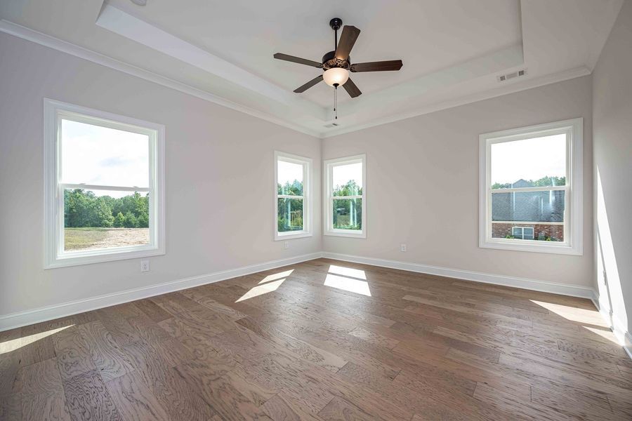 Empty bedroom with wood floors, white walls, and windows. A ceiling fan hangs in the center.