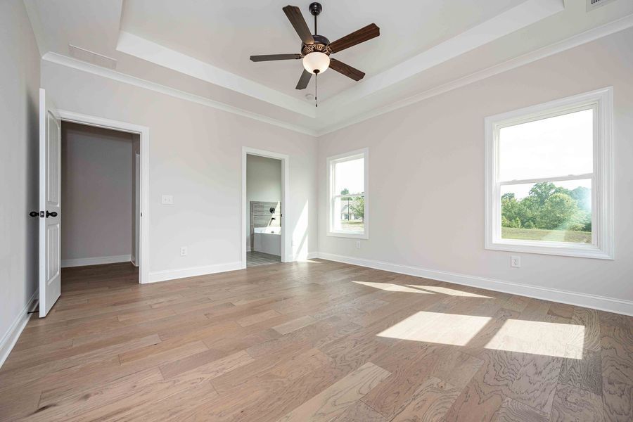 Empty bedroom with light wood floors, windows, ceiling fan, and open doors.