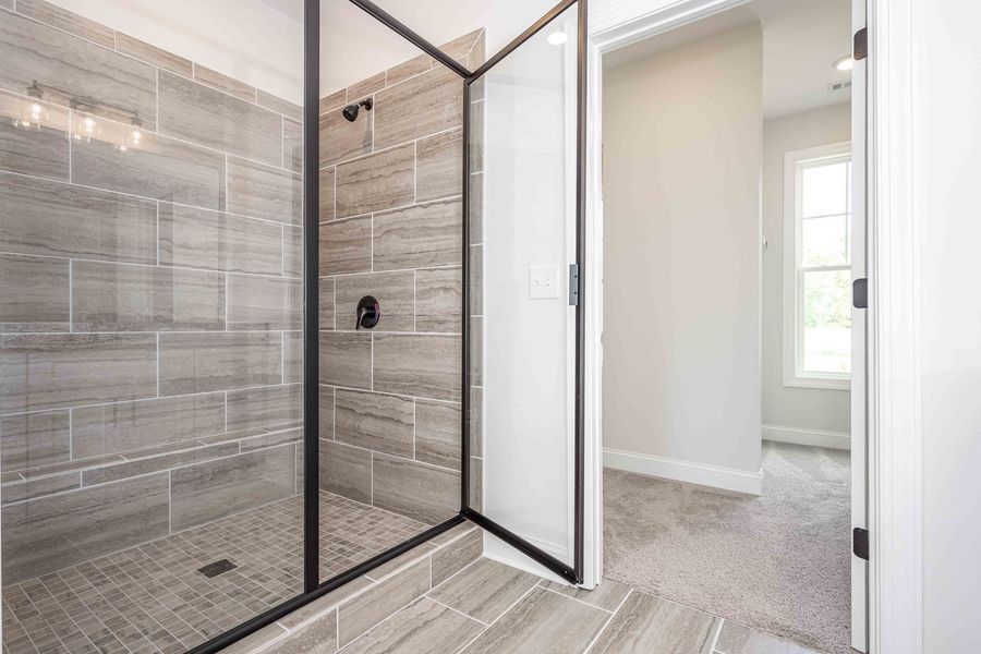 Gray-tiled shower with a black frame and glass door in a neutral-toned bathroom.