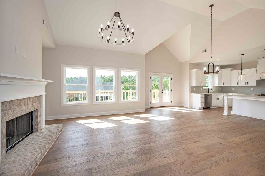 Spacious living area with hardwood floors, fireplace, and high ceilings. Kitchen in the background.