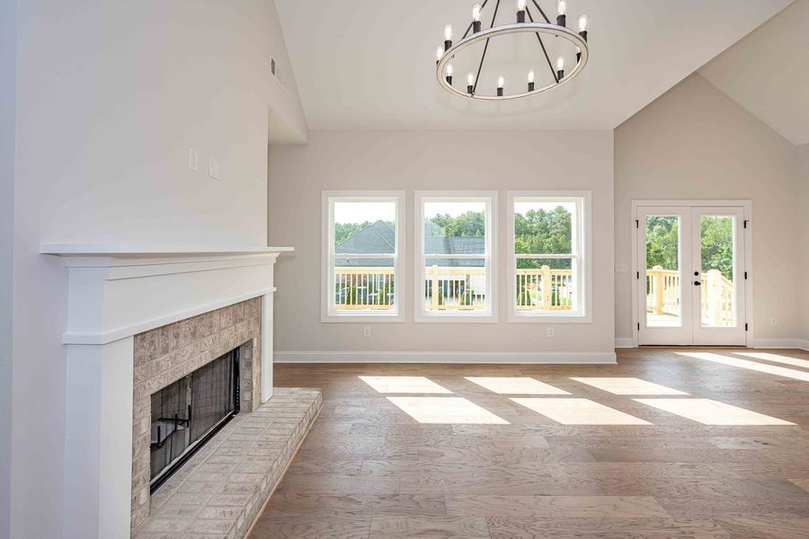 Spacious, sunlit living room with fireplace, windows, and double doors. Features light wood floors and chandelier.