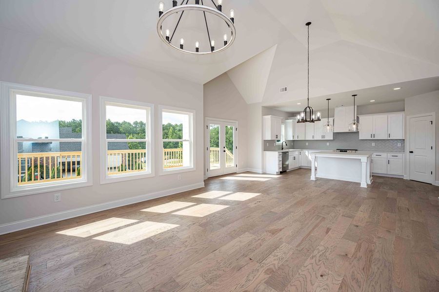 Open-concept living space with wood floors, white walls, kitchen, and large windows overlooking a deck.