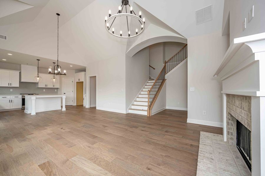 Open-concept living space with kitchen, staircase, and fireplace. Wooden floors, white walls.