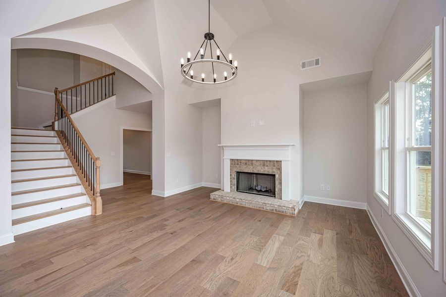 Spacious living room with fireplace, staircase, hardwood floors, high ceiling, and chandelier.