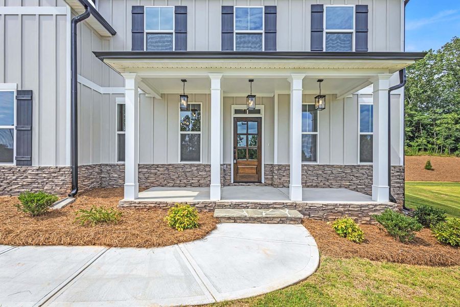 A light gray house with a stone-covered base and a porch with white columns and a brown front door.