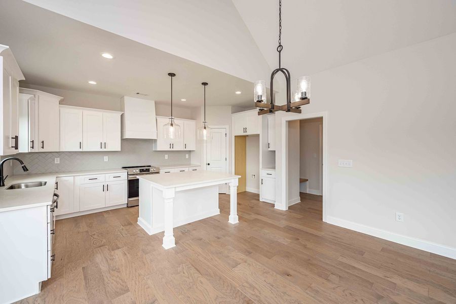 Modern white kitchen with island, wooden floors, and light fixtures.
