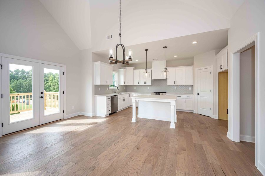 Bright, open kitchen with white cabinets, island, and light wood floors. Double doors lead to a deck.