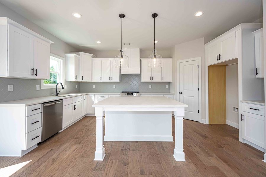 Bright white kitchen with island, cabinets, and stainless steel appliances on hardwood floors.
