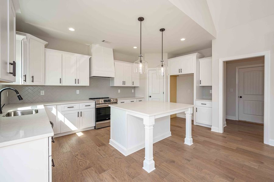 White kitchen with island, white cabinets, stainless steel appliances, and wood flooring.