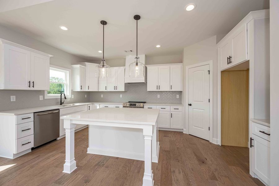 White kitchen with island, cabinetry, stainless steel appliances, hardwood floors.