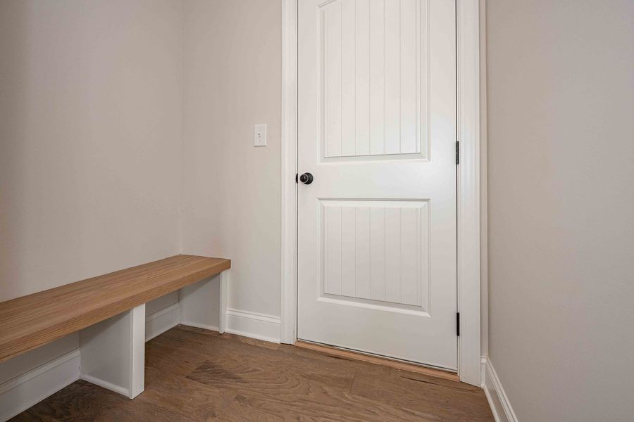 Hallway with wooden bench, white door, and hardwood floor.